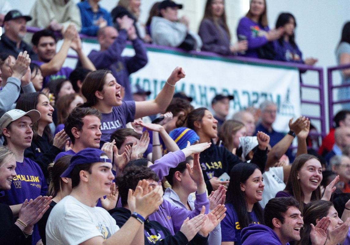 Student fans wearing purple cheer from the stands at a basketball game.